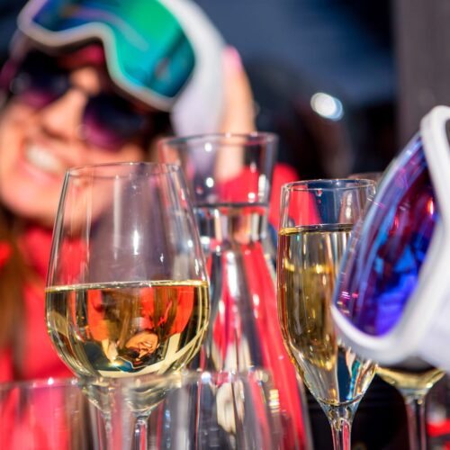 Close-up of wine glasses and ski goggles on a table with colourful clothes in the background.