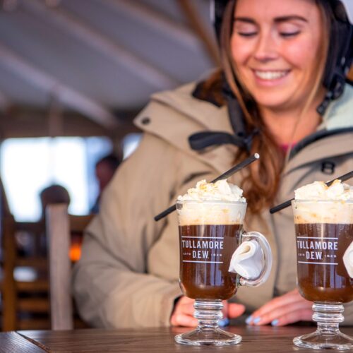 To glas varm chokoladedrik med fløde og sugerør på et træbord indendørs.