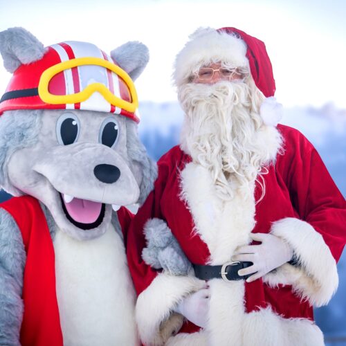 Mascot Vargy in red helmet and waistcoat stands next to Father Christmas in a snowy ski environment