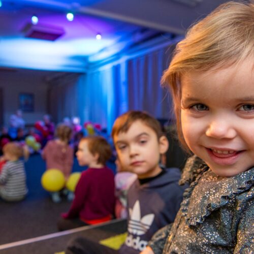 Children sitting on the floor in a room with colourful balloons and blue lights