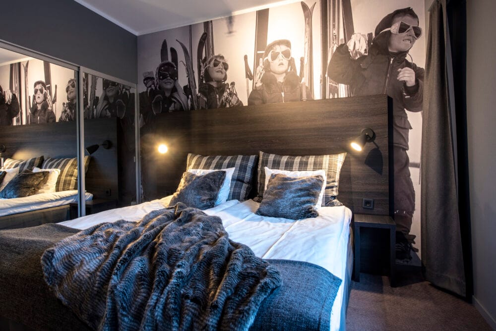 Modern bedroom with double bed, fur blanket, mural with skiers and warm lighting.