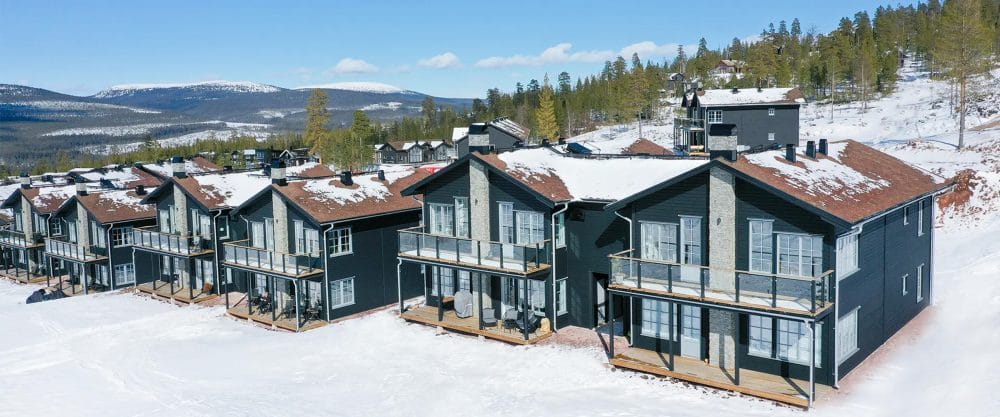 Black mountain houses with snow-covered roofs, large balconies and views of mountains and forests.