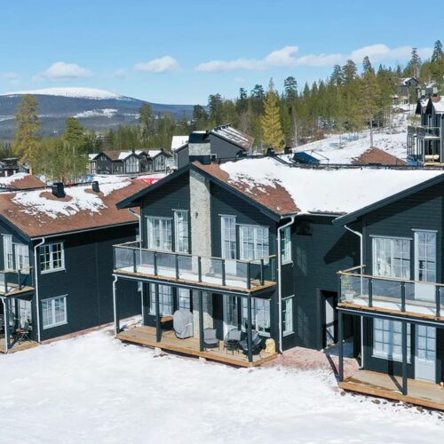 Black mountain houses with snow-covered roofs, large balconies and views of mountains and forests.
