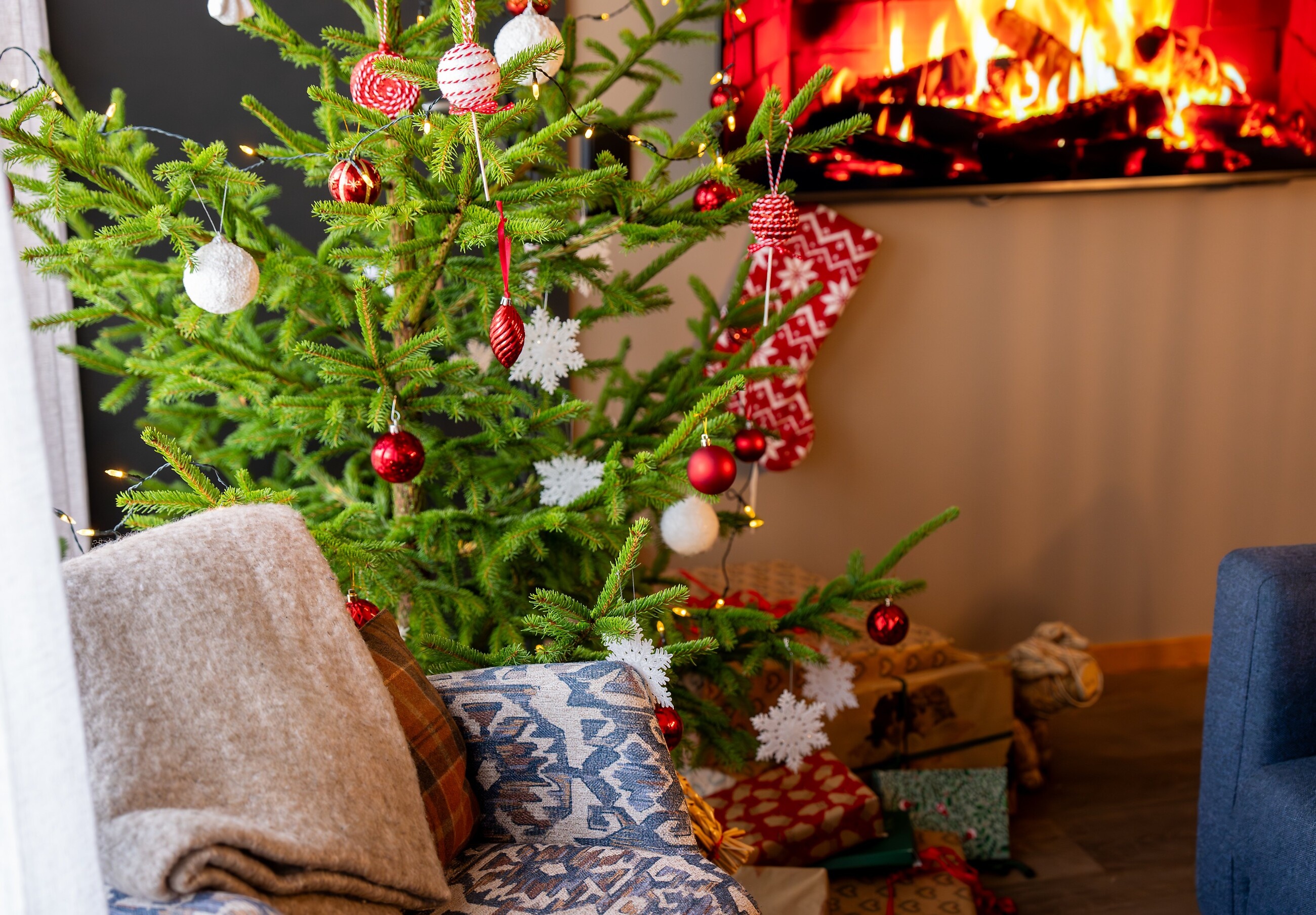 Julgran med julpynt, julklappar och sprakande brasa i julpyntat vardagsrum.