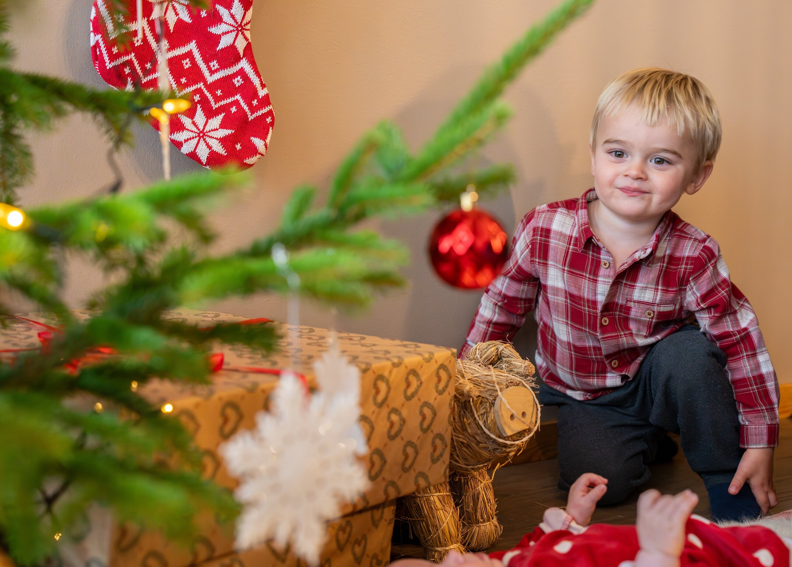 Barn sitter vid julgran och julklappar i julpyntat vardagsrum.