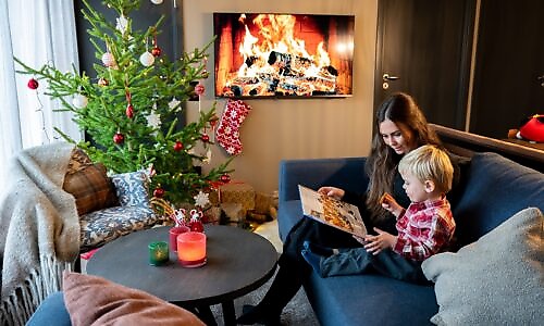 A person and a child are reading a book in a living room decorated for Christmas.