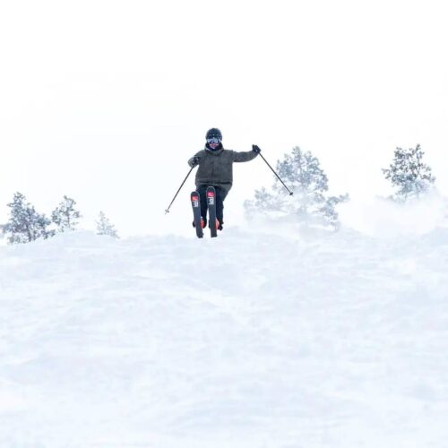 Three people skiing down a snow-covered slope, jumping with skis and swinging in powder snow