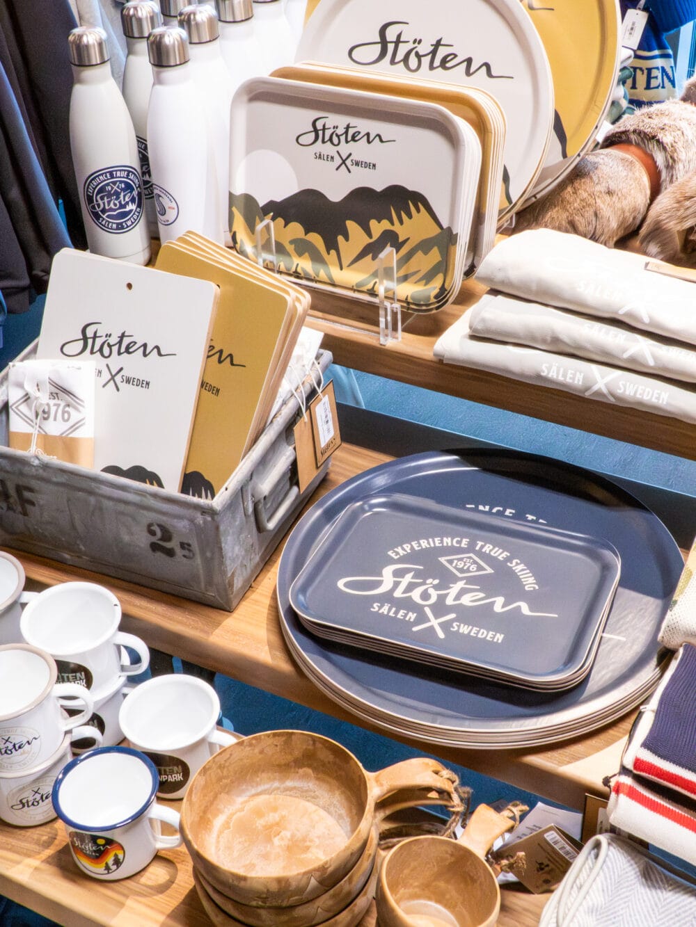 Butikshylla med Stöten‑produkter, brickor, flaskor, muggar och textilier i trädisplay.