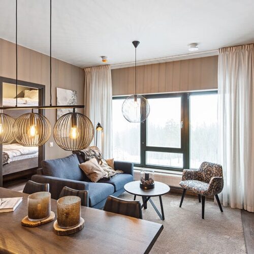 Modern living room with large windows, grey sofa, dining table and decorative metal pendant lights.