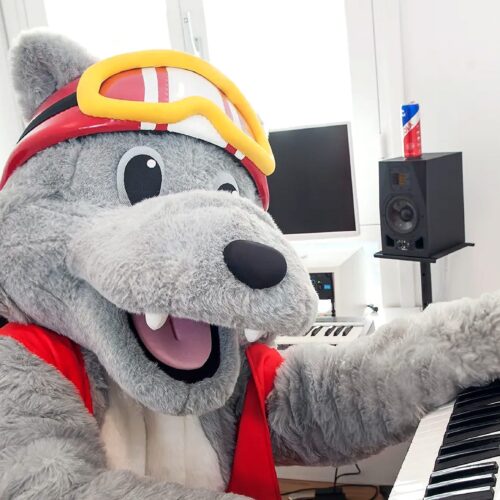 Maskotten Vargy spiller på et hvidt keyboard i et musikstudie med højttalere