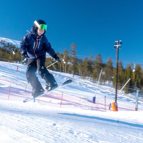 Person hopper med snowboard på skibakke med snedækkede pister og solrigt vejr