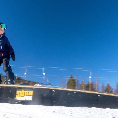 Person snowboarding on rail in sunny ski area with blue sky and snow