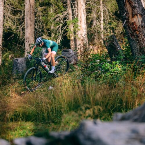 Cyklist i grönt ställ kör mountainbike på smal stig genom tät skog med högt gräs.