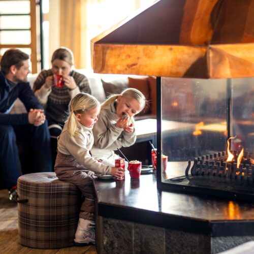 Familien sidder ved pejsen og drikker varme drikke i røde krus på loungebordet.