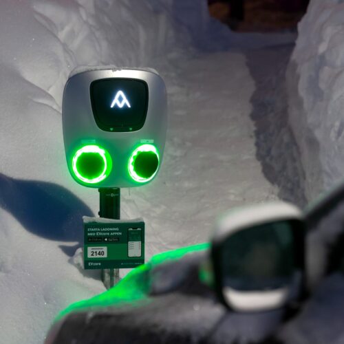 Grønt oplyst ladestation til elbiler omgivet af dyb sne på en oplyst gangsti.