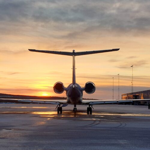 Private jet standing on the airport runway at sunset with hangar and staff in the background.