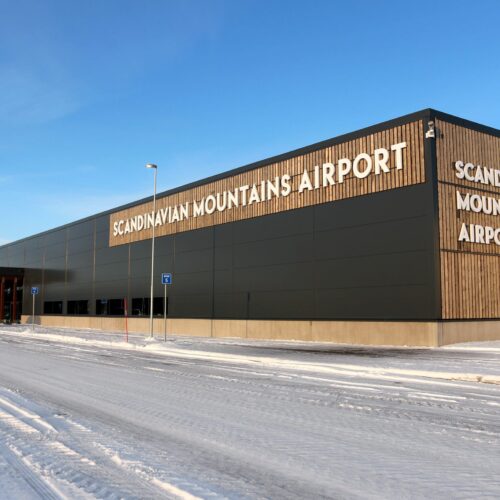 Scandinavian Mountains Airport building with wood panelling and snow-covered ground under a clear blue sky.