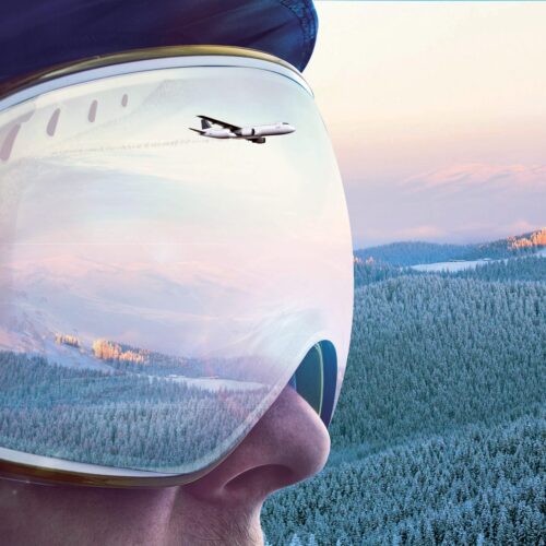 Aeroplanes reflected in ski goggles overlooking snow-capped mountains and forests.