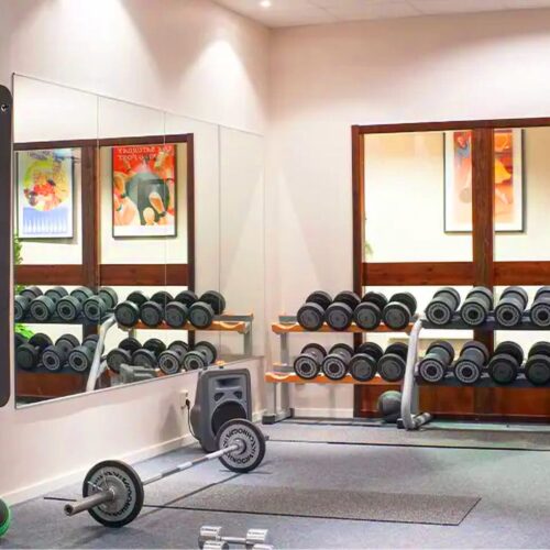 Moderne fitnesscenter med træningsmaskiner, frie vægte og spejlvæg under kraftig loftsbelysning.