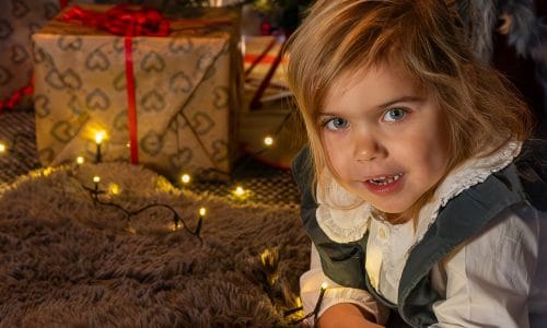 Children lying on a mat reading a book in front of a Christmas tree with tinsel and wrapped presents