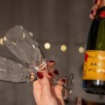 Two champagne glasses are raised next to a bottle of cava with festive backlighting