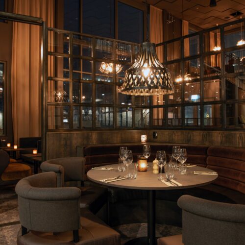 Elegant dining area with round seating, table setting, glassware, candles and decorative lamp.