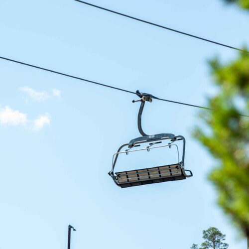 Tom stolelift hængende mod klar blå himmel med slørede træer i forgrunden