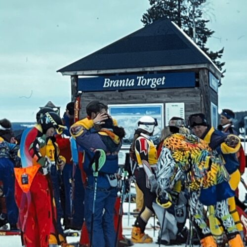 Grupp skidåkare samlade vid Branta Torget med färgglada kläder och utrustning i snötäckt fjällmiljö.