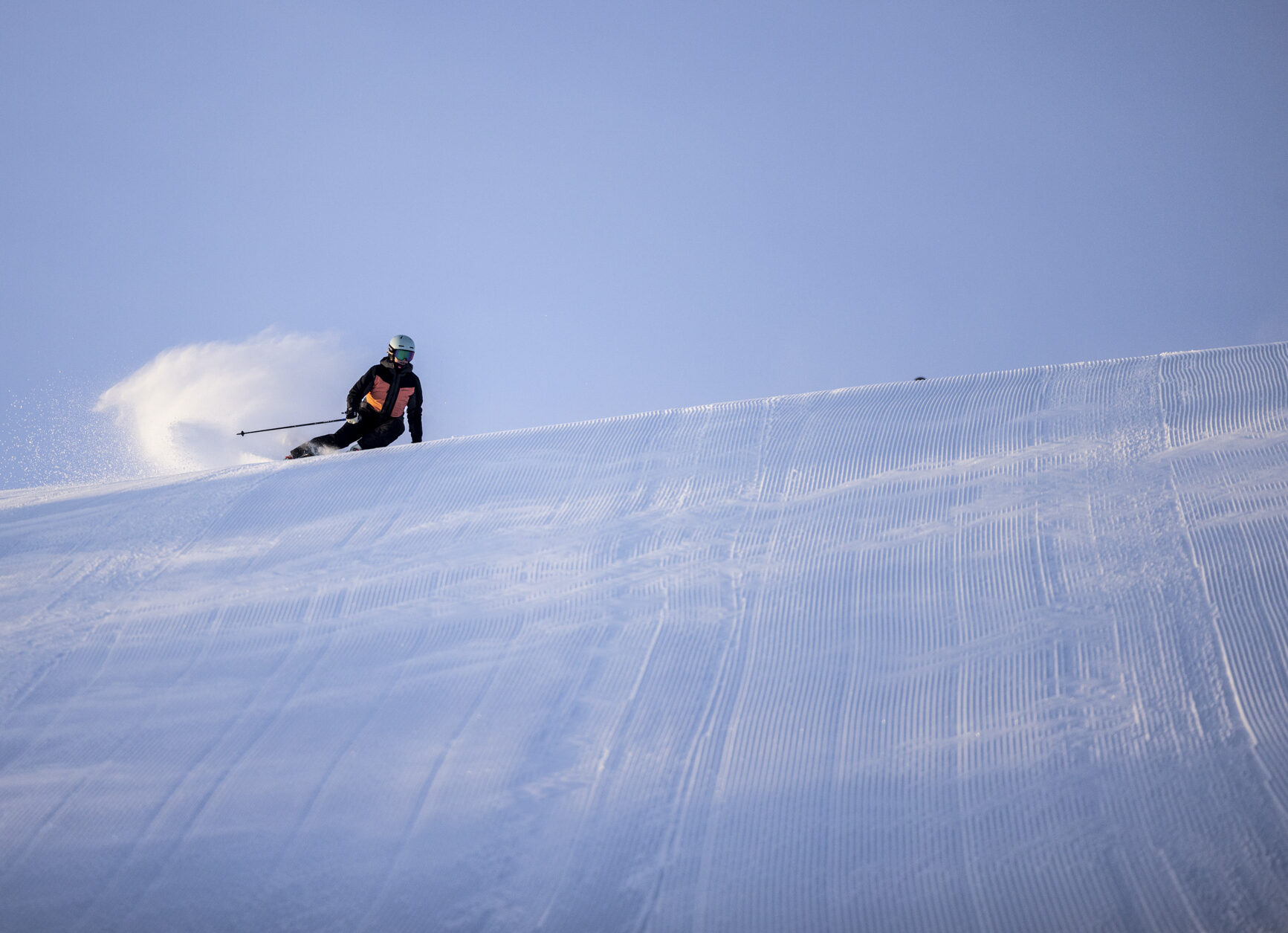 Skidåkare svänger i pudersnö på pist med blå himmel och snö som virvlar upp