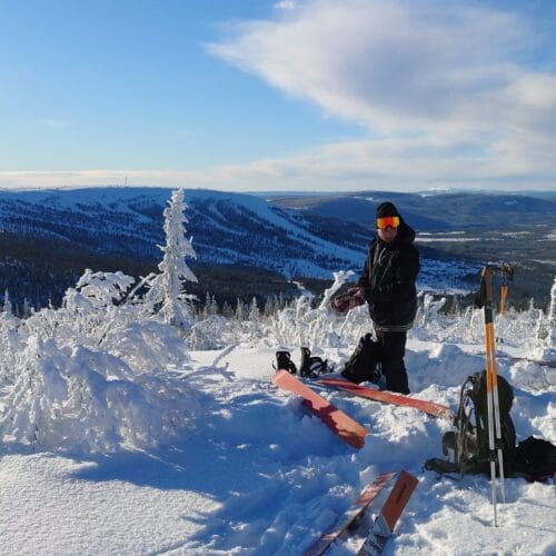 To personer forbereder ski i et snedækket bjergmiljø med udsigt over dal og bjerge.