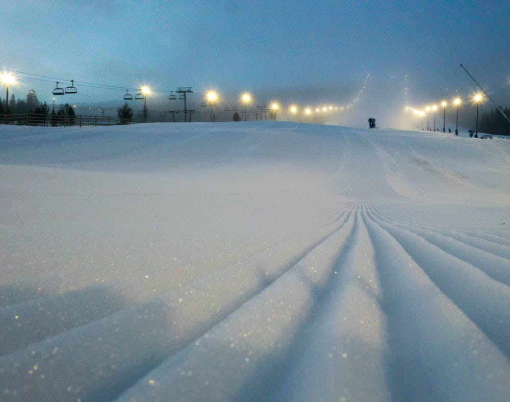 Nypistad skidbacke i dimma med upplysta lampor och lift i bakgrunden.
