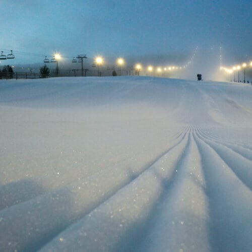 Nypræpareret skibakke i tåge med oplyste lys og lift i baggrunden.