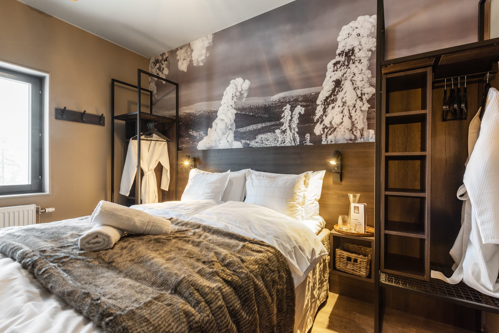 Hotelseng med belysning og badekåbe hængende på siden.