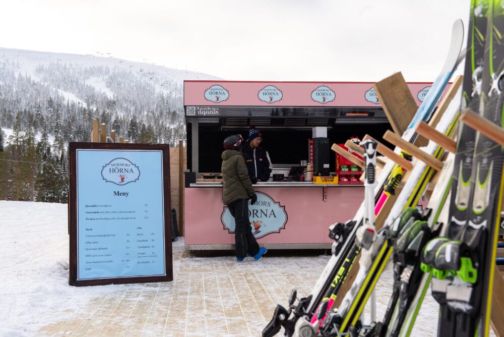 Uteservering vid skidbacke där en person beställer mat vid en rosa kiosk.