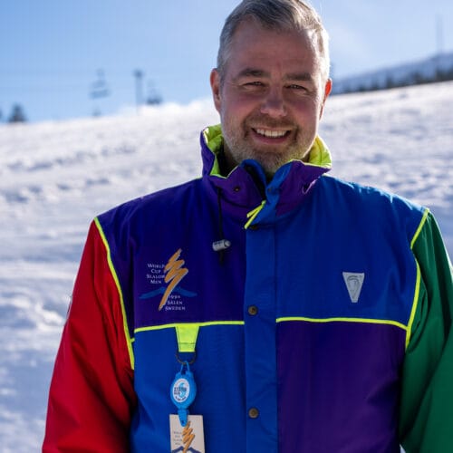 Happy person wearing a colourful jacket in front of a sunny ski slope