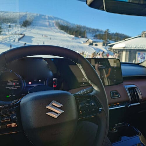 Bil invändigt med vy över en solig skidbacke.
