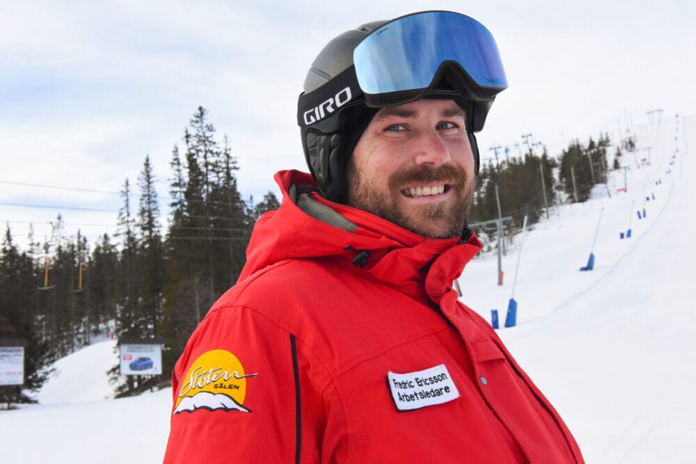 Skidlärare iklädd röd uniform och skidhjälm i en skidbacke.