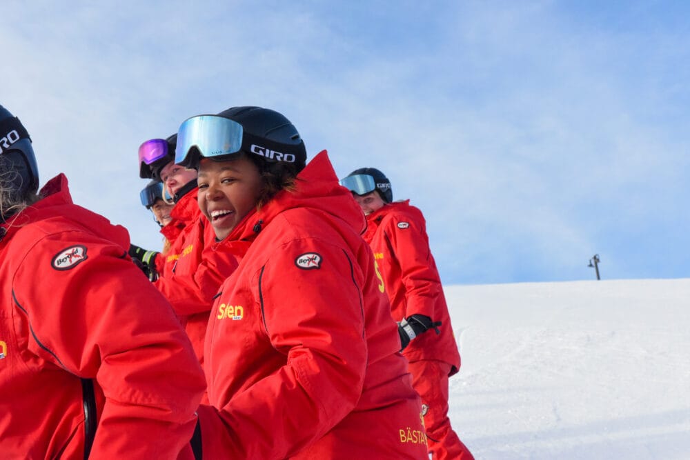 Several ski instructors are standing on a ski slope wearing red ski suits.