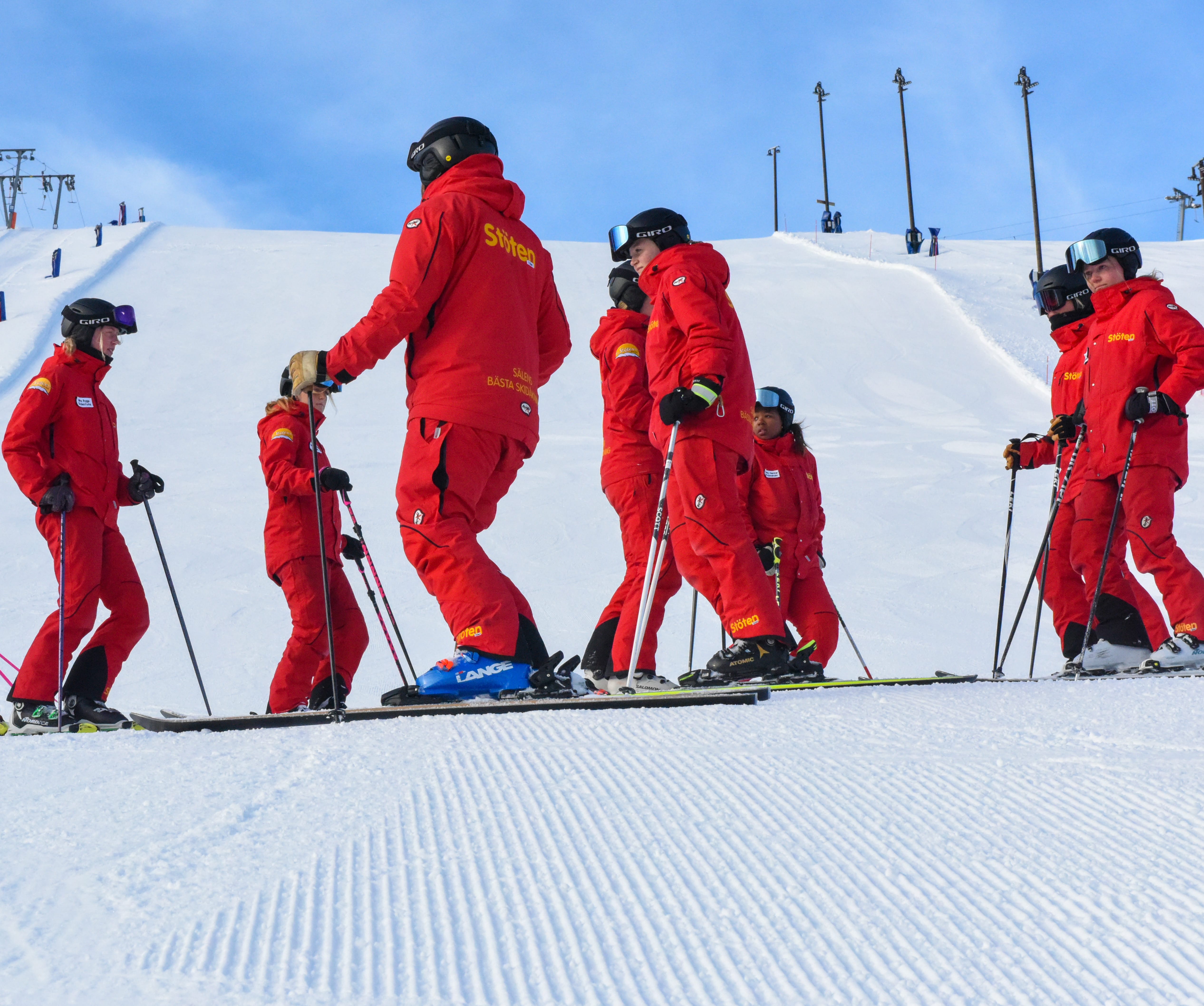 Ski instructors in red uniforms talking on a ski slope.