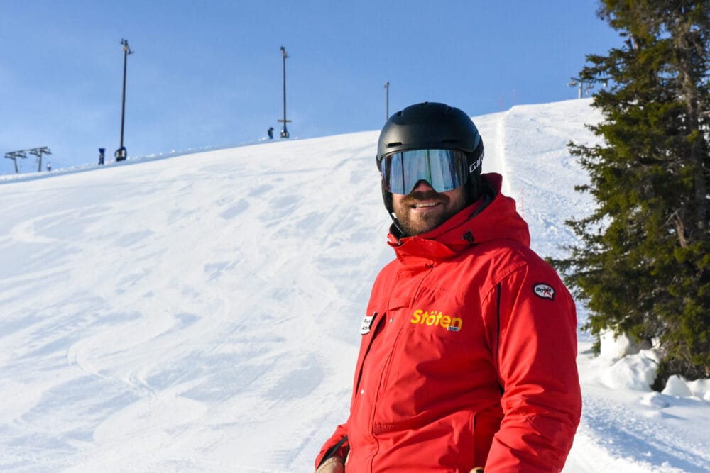 Ski instructor standing in red uniform with ski goggles on sunny ski slope.