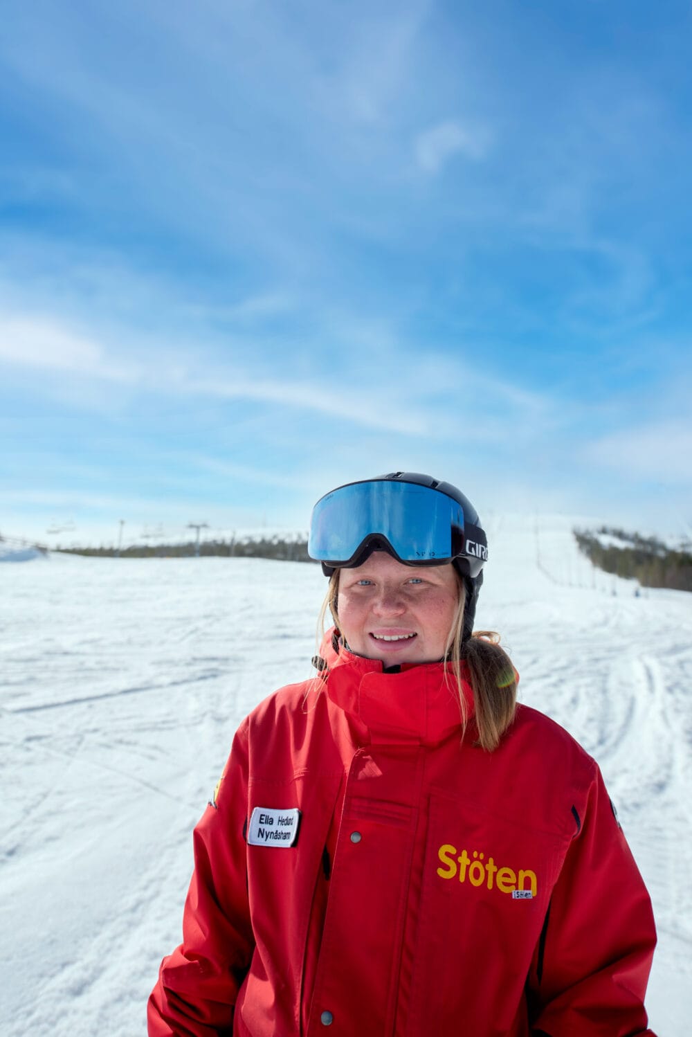 Skidlärare i röd uniform med hjälm och skidglasögon i ett skidlandskap.