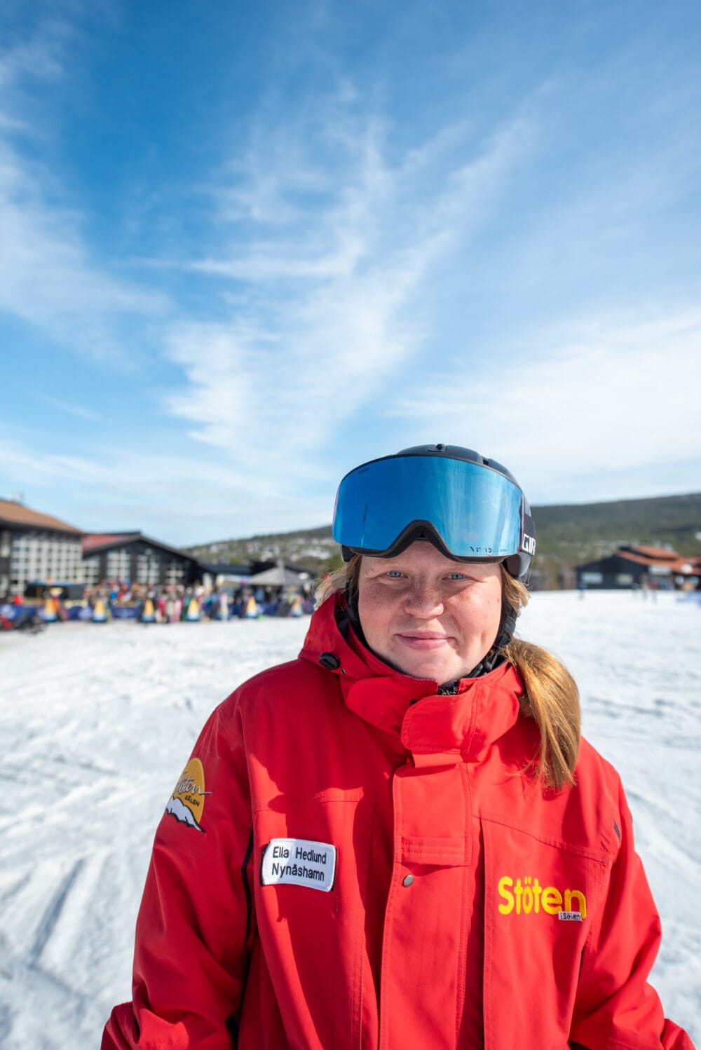 Skidlärare i röd uniform med hjälm och skidglasögon i ett skidlandskap.