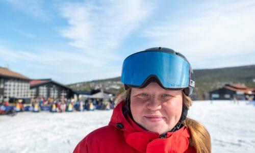 Skilærer i rød uniform med hjelm og skibriller i et skilandskab.