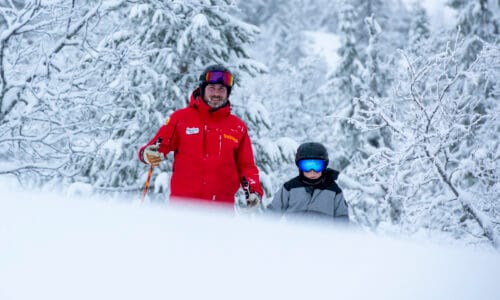 Ski instructors and children standing in a snow-covered forest.