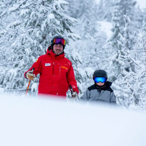 Skilærere og børn står i en snedækket skov.