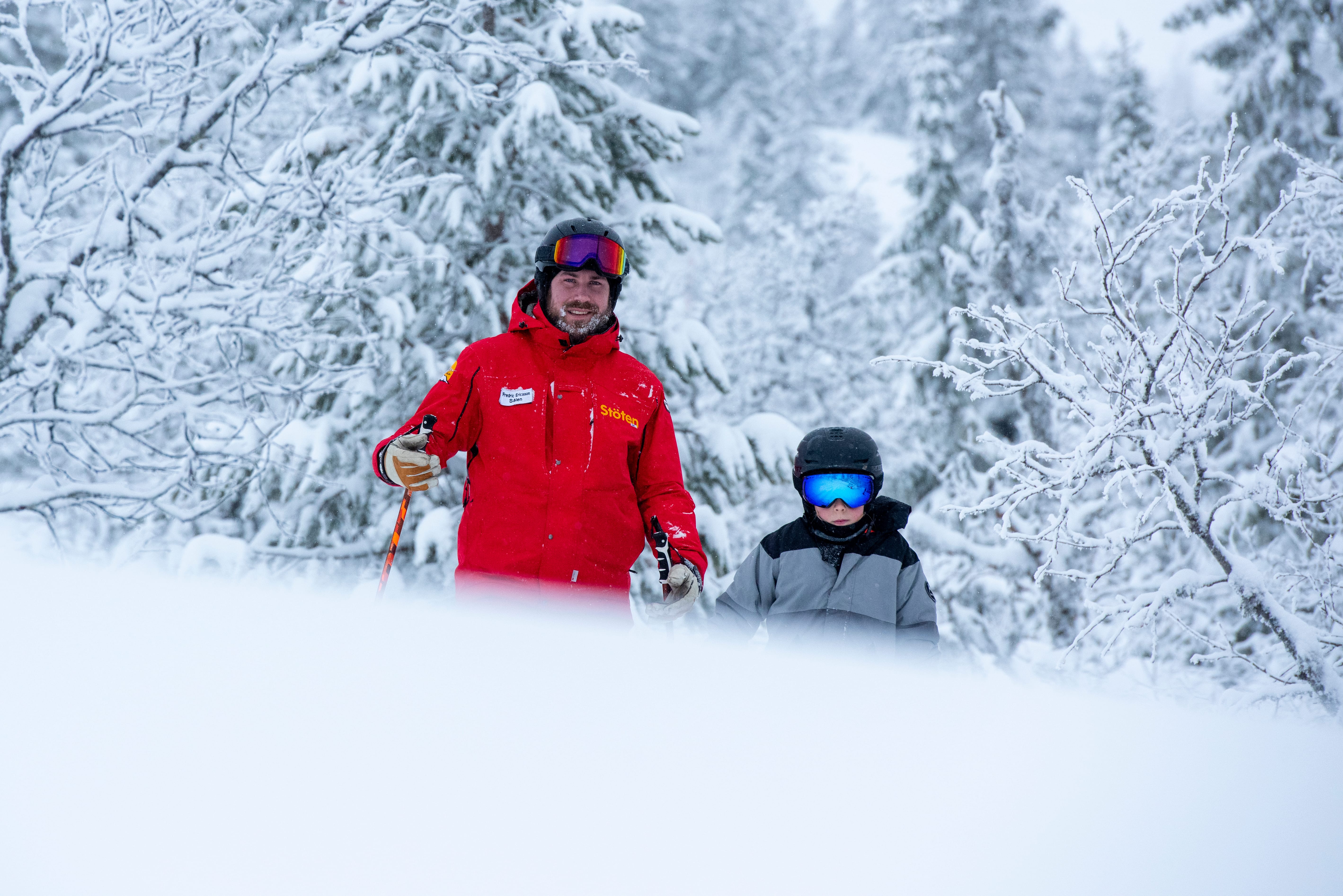Ski instructors and children standing in a snow-covered forest.