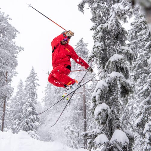 Skidlärare hoppar på skidor i en snöklädd skog.