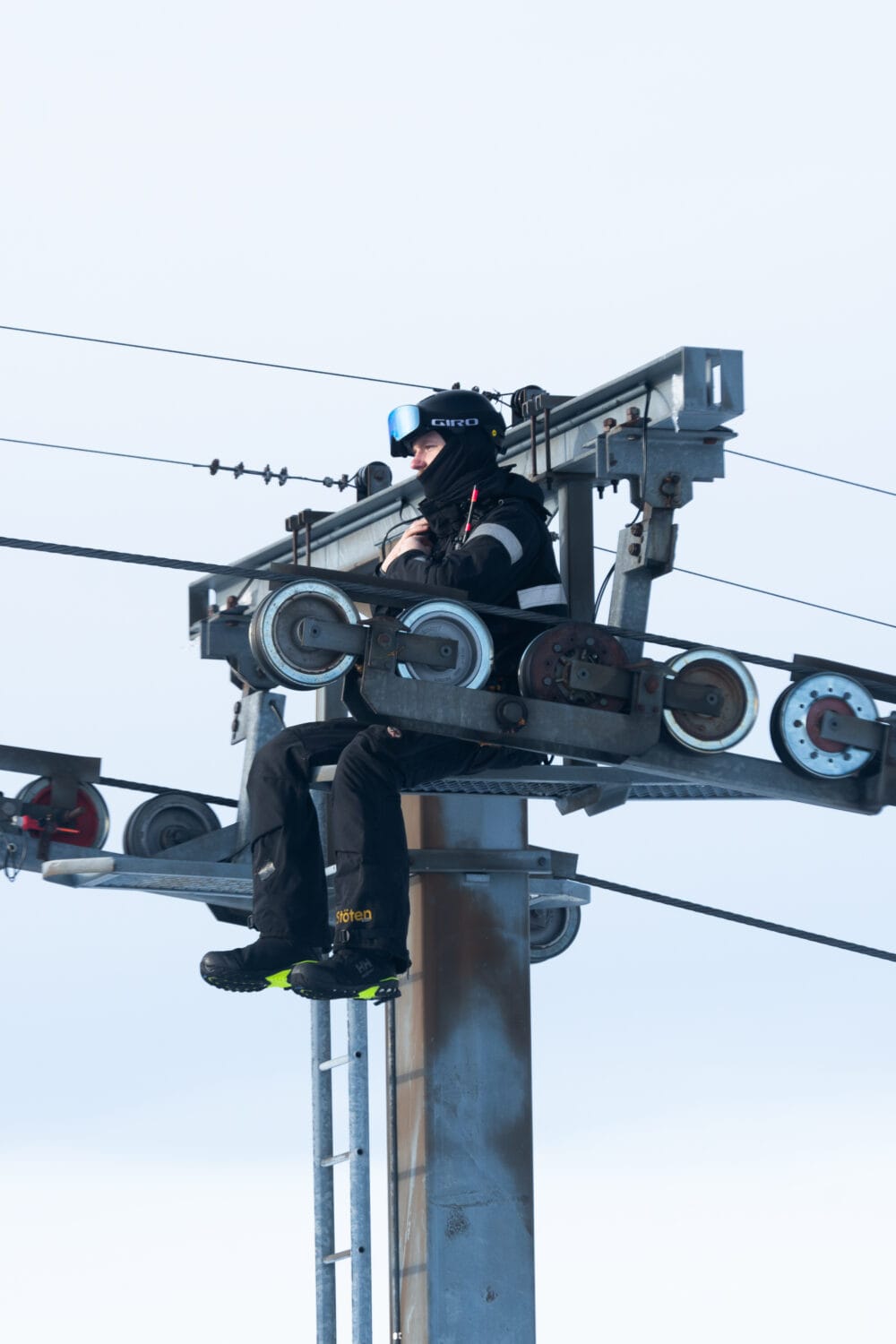 Mechanics sitting on a lift mast working with blue sky in the background.
