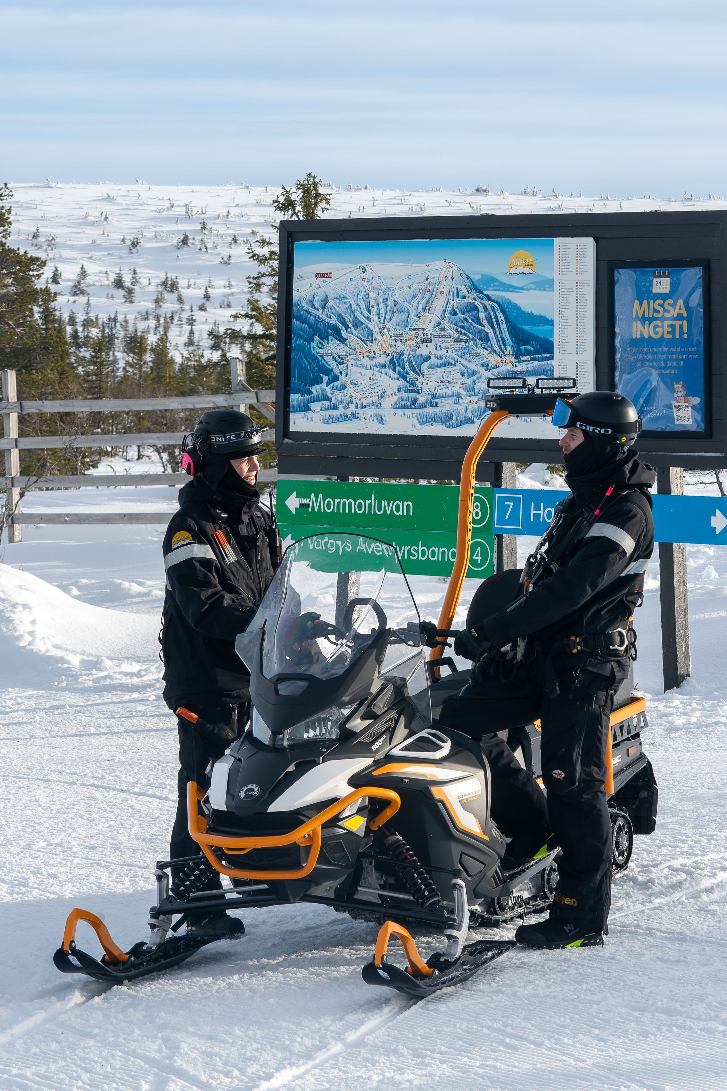 Mechanic standing by a snowmobile in front of a piste map.