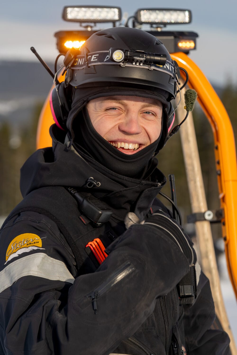 Mechanic in black uniform on snowmobile smiles at the camera.